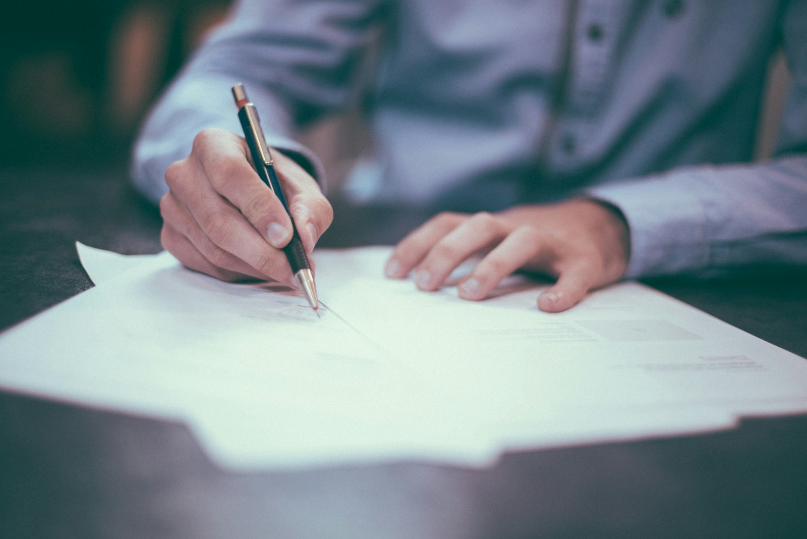 Hands completing paper claim forms with a pen